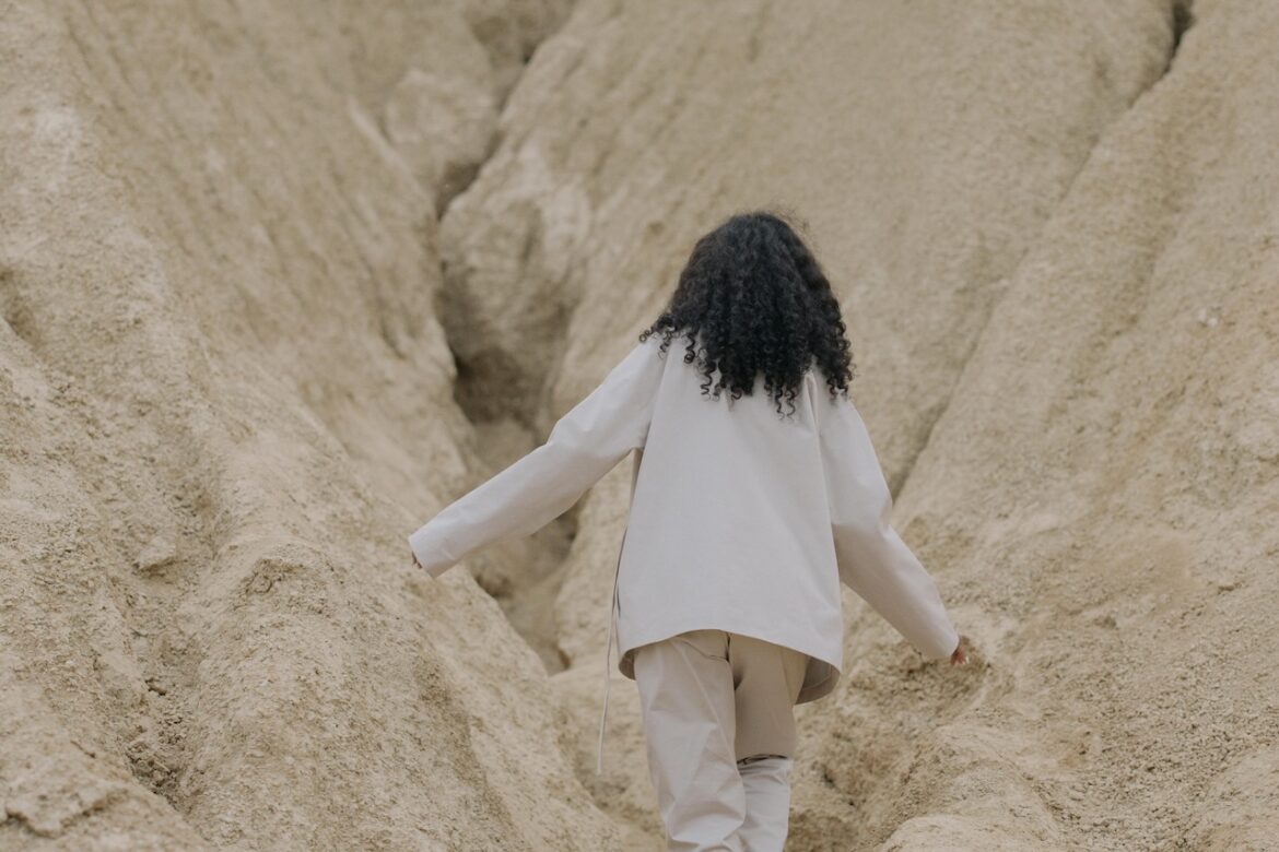 Woman walkiing between two stone walls symbolizing the that often uncomfortable space between selves when you are in transition.